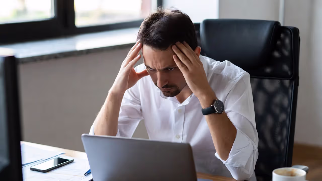 Stressed office worker sitting at a desk with a laptop and documents in a modern office