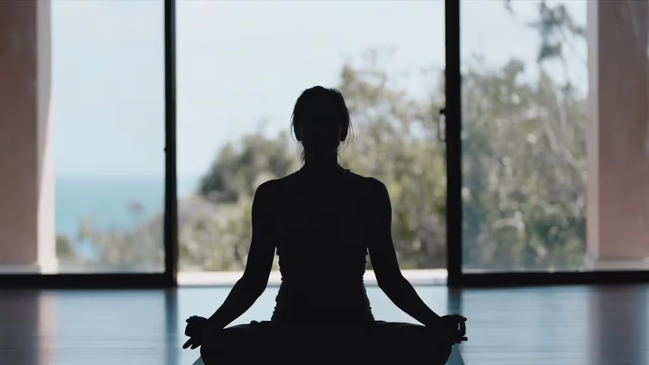 Adult meditating in a bright retreat space with large windows overlooking nature