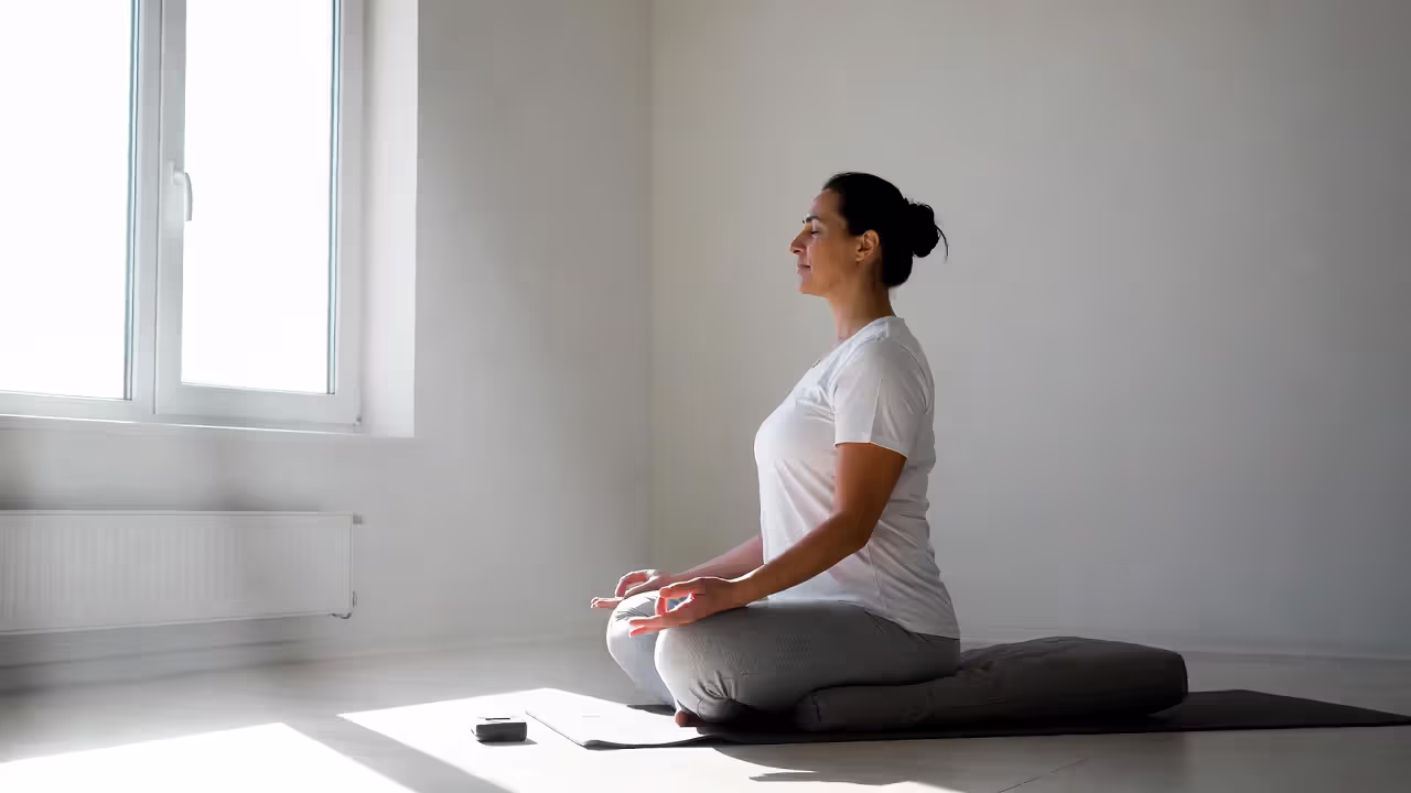 Person meditating on a cushion in a bright minimalist room with a timer nearby