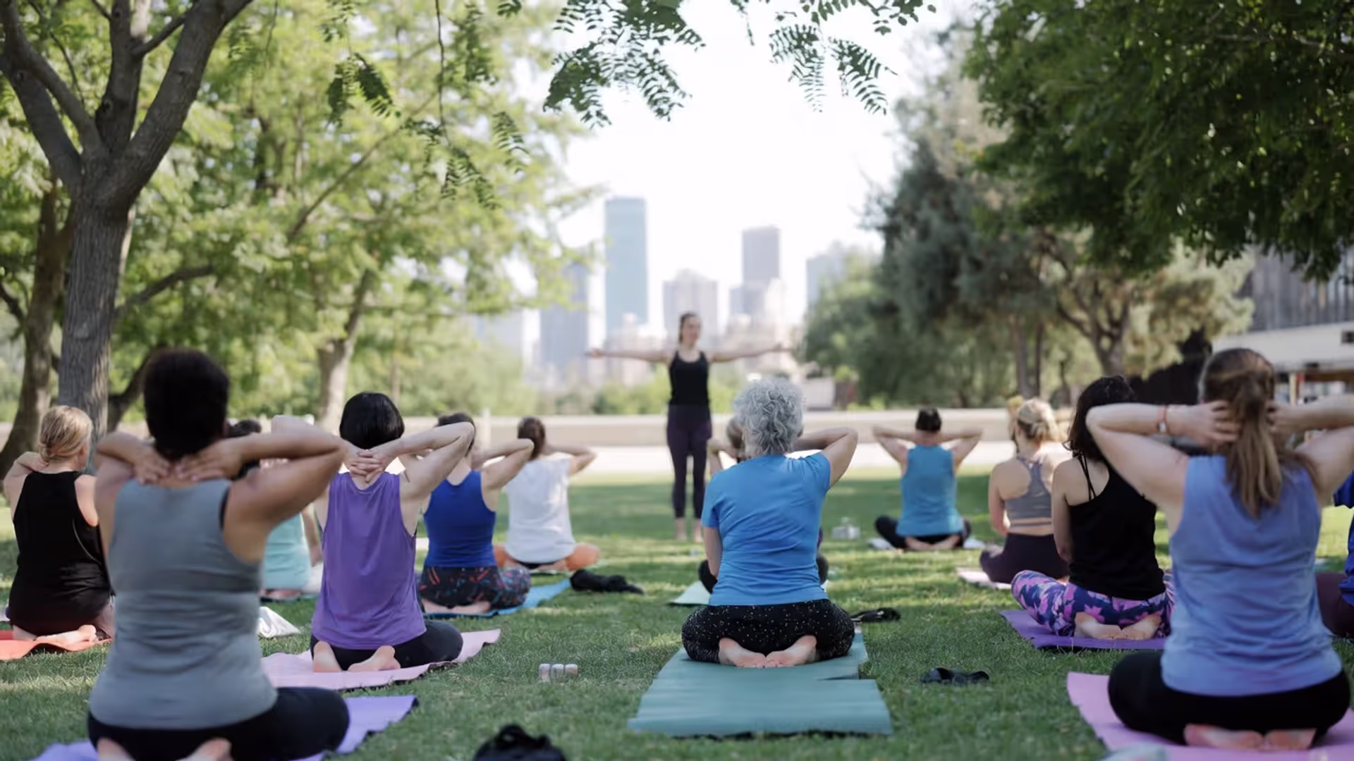 Group of people practicing free outdoor yoga in a city park with an instructor leading.