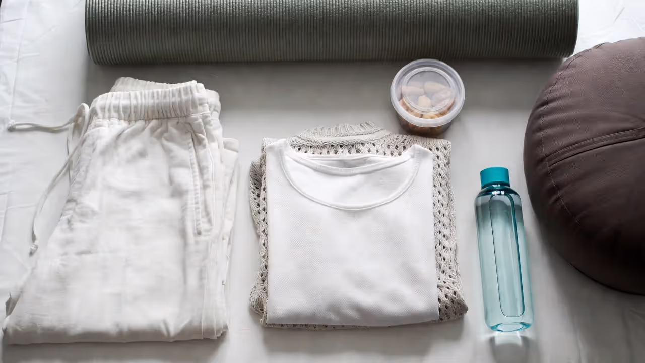 White clothing, cushion, mat, and water bottle laid out as preparation for a white tantric yoga event.
